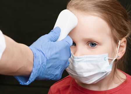 Pediatrician or doctor checks little girl's body temperature using infrared forehead thermometer...