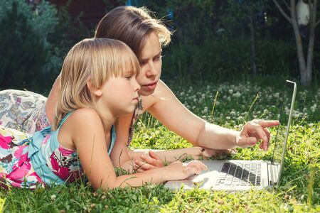 Mother helping her little daughter to use laptop computer. Child studying at home doing her homework or having online lesson. Homeschooling conceptの写真素材