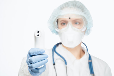 Close-up shot of doctor wearing protective suit and surgical mask holding infrared forehead...