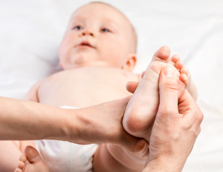 Five month baby boy receiving massage therapy in pediatric clinic. Manual therapist manipulates childs's footの写真素材