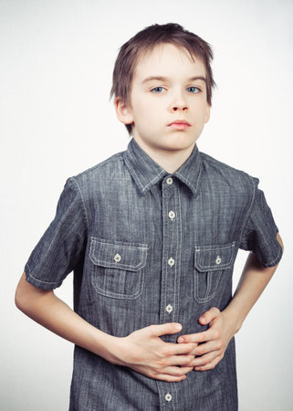 Portrait of sad schoolboy holding his hands on stomach suffering from abdominal painの写真素材