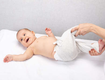 Happy six month baby girl receiving massage therapy in pediatric clinic. Manual therapist manipulates child's legs and hipsの写真素材