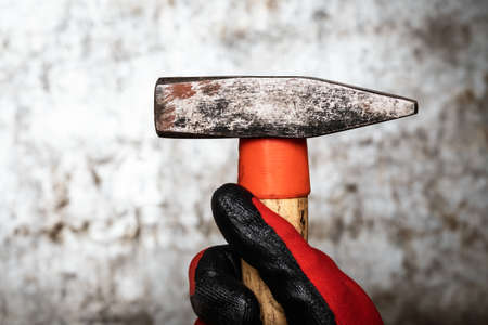 Person wearing protective glove holding a hammer against metal background