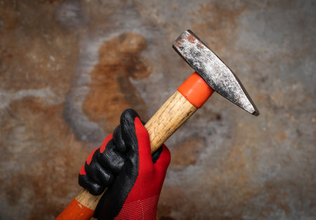 Person wearing protective glove holding a hammer against rusty metal backgroundの写真素材