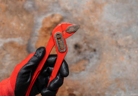 Mechanic or plumber wearing protective glove holding red adjustable pliers against rusty metal backgroundの写真素材