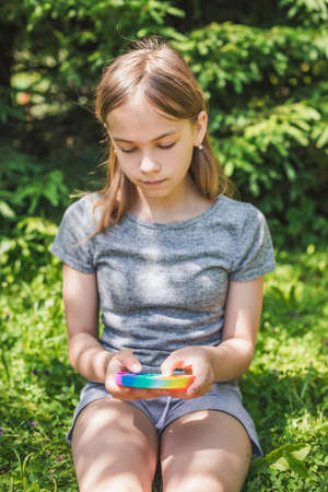 Preteen girl playing silicone antistress popit fidget toy outdoors, focus on fidgetの写真素材