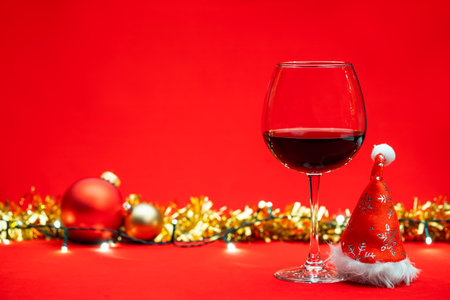 Glass of red wine with christmas baubles tinsel and lights on red background - christmas drink conceptの写真素材