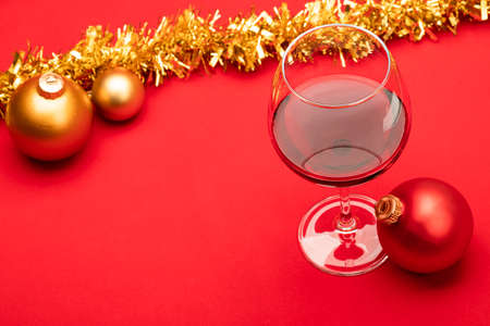 Glass of red wine with christmas baubles and tinsel on red background - christmas drink conceptの写真素材