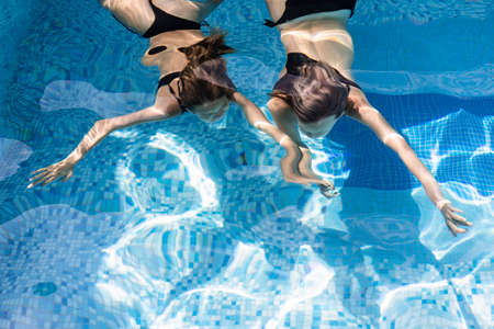 Teenage girls swimming underwater in a hotel pool enjoying summer holidaysの写真素材