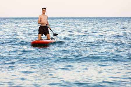 Teenager boy learning to paddle on a SUP board in the sea kneeling