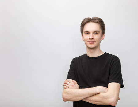 Portrait of cheerful young man wearing black tshirt standing with arms crossed smiling at camera. Studio shot on gray backgroundの写真素材