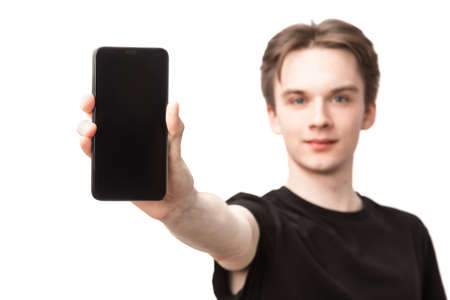 Portrait of young man wearing black tshirt showing smartphone, focus on a phone. Studio shot on white backgroundの写真素材