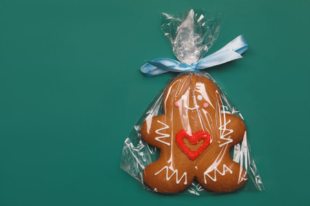 Iced Christmas Gingerbread man sugar cookie with red heart wrapped in plastic on green backgroundの写真素材