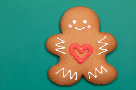 Christmas Gingerbread man sugar cookie in humanoid shape with red heart icing decoration on green backgroundの写真素材