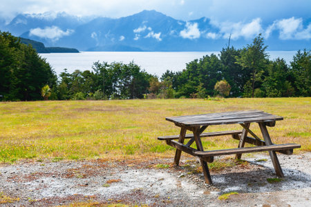 Wooden picnic table overloking scenic Manapouri Lake and mountain range of Fiordland National Park in Southland, South Island of New Zealandの写真素材