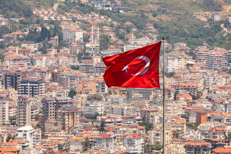 Waving Turkish flag on a flagpole with urban development in background, Alanya, Turkeyの写真素材