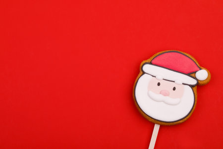 Festive Santa Claus-shaped gingerbread cookie pop with white icing on red backgroundの写真素材
