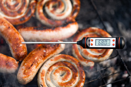 Ð¡lose-up shot of a digital meat thermometer displaying a safe cooking temperature of sausages cooking on a smokey grillの写真素材