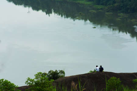 two friends sitting on the top of rock mountain and looking over the valley river