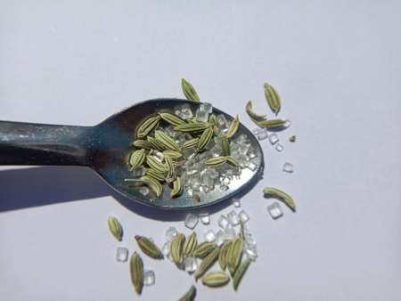 isolated white background picture of green fennel saunf and sugar on spoon