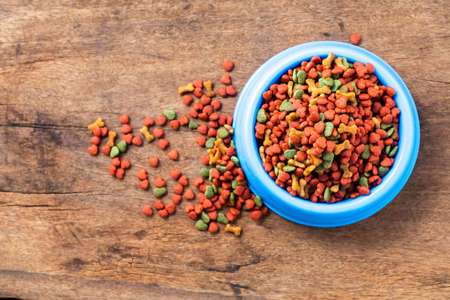Yellow plastic bowl full with dry dog food isolated on white background. Top view grain pet food...