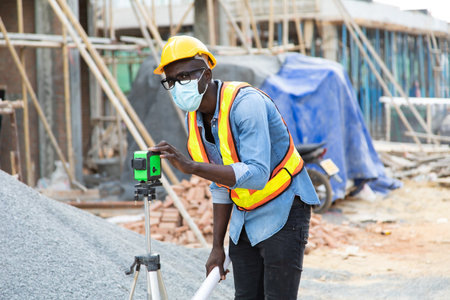 African American construction worker on building site. wearing surgical face mask during coronavirus...