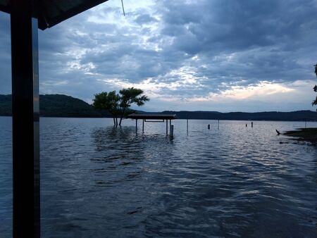 Submerged benches and tree in an artificial lake that has flooded the coast during cloudy eveningの写真素材