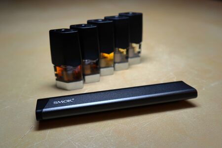 Smok Infinix refillable pod vape pen electronic cigarette with pods filled with e-juices of different shades of orange arranged in a gradient, isolated close upのeditorial素材