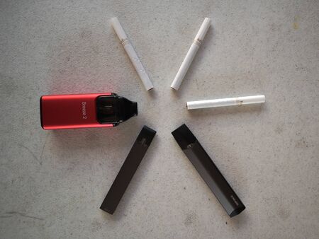3 vape electronic cigarette juul, aspire breeze, smok inifinix devices and 3 marlboro gold light cigarettes in a star pattern on a white textured background isolateのeditorial素材