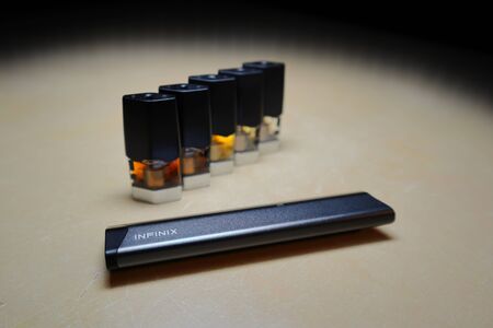 Smok Infinix refillable pod vape pen electronic cigarette with pods filled with e-juices of different shades of orange arranged in a gradient, isolated close upのeditorial素材