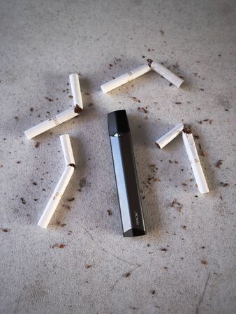 Vape device electronic cigarette smok infinix, as smoking alternative with broken marlboro gold cigarettes and scattered tobacco on white textured backgroundのeditorial素材