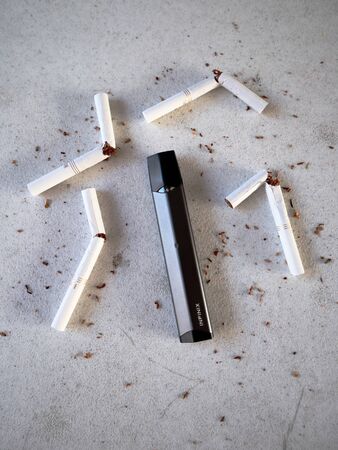 Vape device electronic cigarette smok infinix, as smoking alternative with broken marlboro gold cigarettes and scattered tobacco on white textured backgroundのeditorial素材