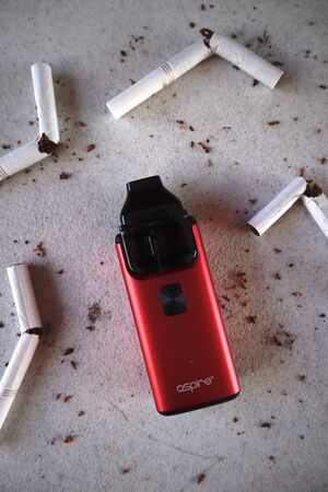 Vape device electronic cigarette aspire breeze, as smoking alternative with broken marlboro gold cigarettes and scattered tobacco on white textured backgroundのeditorial素材