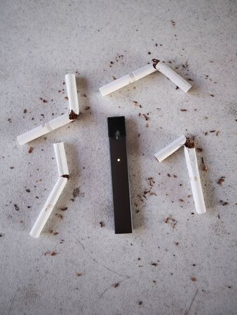 Vape device electronic cigarette juul, as smoking alternative with broken marlboro gold cigarettes and scattered tobacco on white textured backgroundのeditorial素材