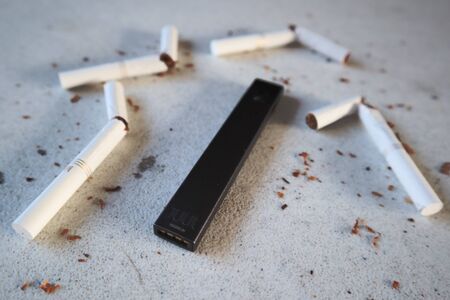 Vape device electronic cigarette juul, as smoking alternative with broken marlboro gold cigarettes and scattered tobacco on white textured backgroundのeditorial素材