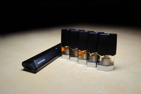Smok Infinix refillable pod vape pen electronic cigarette with pods filled with e-juices of different shades of orange arranged in a gradient, isolated close upのeditorial素材