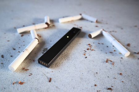 Vape device electronic cigarette juul, as smoking alternative with broken marlboro gold cigarettes and scattered tobacco on white textured backgroundのeditorial素材