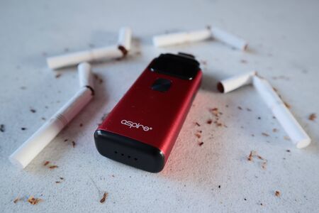 Vape device electronic cigarette aspire breeze, as smoking alternative with broken marlboro gold cigarettes and scattered tobacco on white textured backgroundのeditorial素材