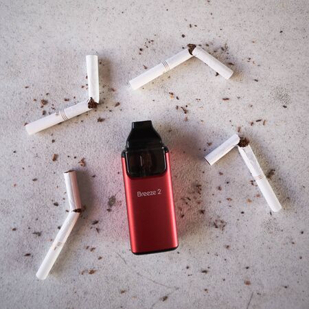 Vape device electronic cigarette aspire breeze, as smoking alternative with broken marlboro gold cigarettes and scattered tobacco on white textured backgroundのeditorial素材