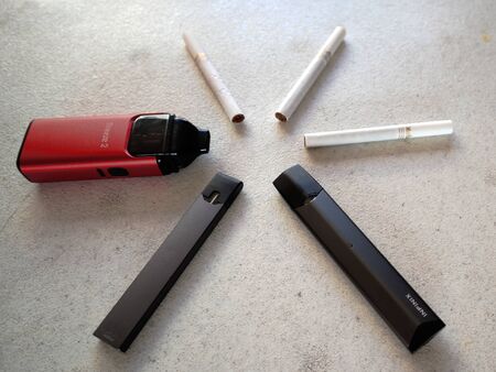3 vape electronic cigarette juul, aspire breeze, smok inifinix devices and 3 marlboro gold light cigarettes in a star pattern on a white textured background isolateのeditorial素材