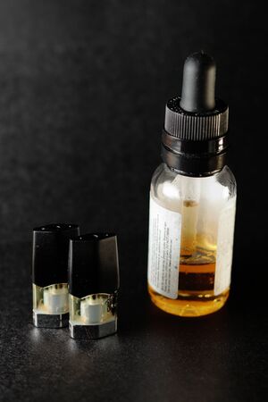 e-juice vape refill pods with with a bottle of orange e-liquid, isolated close up black backgroundの写真素材
