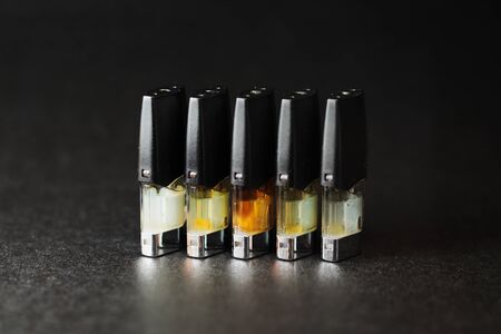 e-juice vape refill pods with liquids of different shades of orange yellow, black background isolated close upの写真素材
