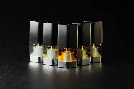 e-juice vape refill pods with liquids of different shades of orange yellow, black background isolated close upの写真素材