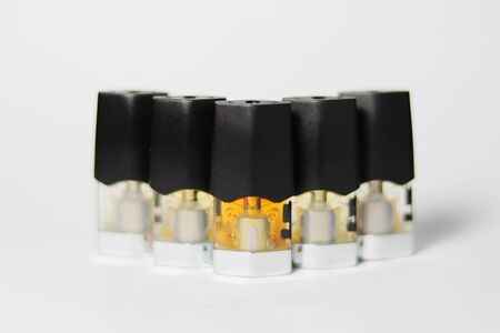 e-juice vape refill pods with liquids of different shades of orange yellow, white background shallow focusの写真素材