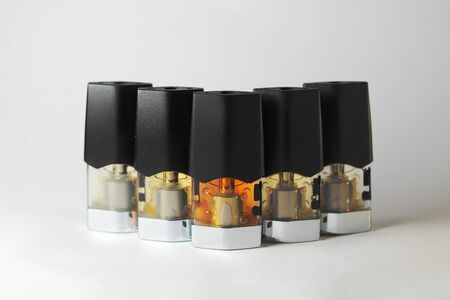 e-juice vape refill pods with liquids of different shades of orange yellow, white background isolated close upの写真素材