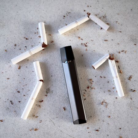 Single vape pen type electronic cigarette as smoking alternative with broken cigarettes and scattered tobacco on white textured background isolatedの写真素材