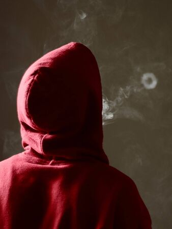 Young male in red hoodie vaping smoking, blows a single smoke ring, isolated rear viewの写真素材