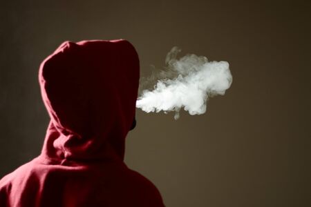 Young male in red hoodie vaping smoking, exhales thick vapor, isolated rear viewの写真素材