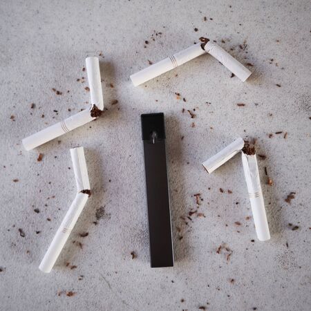 Single vape pen type electronic cigarette as smoking alternative with broken cigarettes and scattered tobacco on white textured background isolatedの写真素材