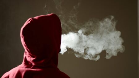 Young male in red hoodie vaping smoking, exhales thick vapor, isolated rear viewの写真素材